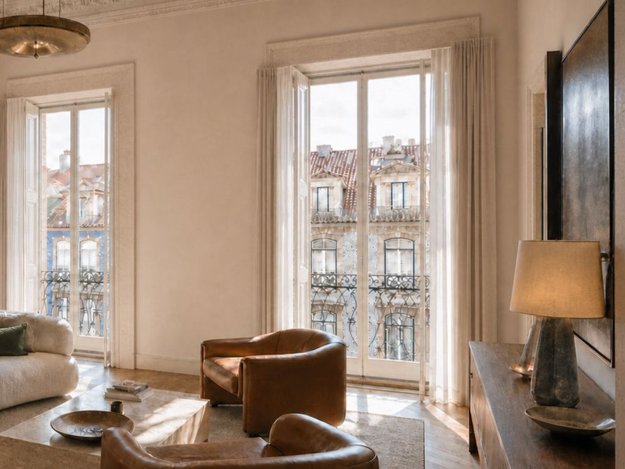 The living room of a Lisbon apartment: leather armchairs, a shaded lamp and full-height windows.