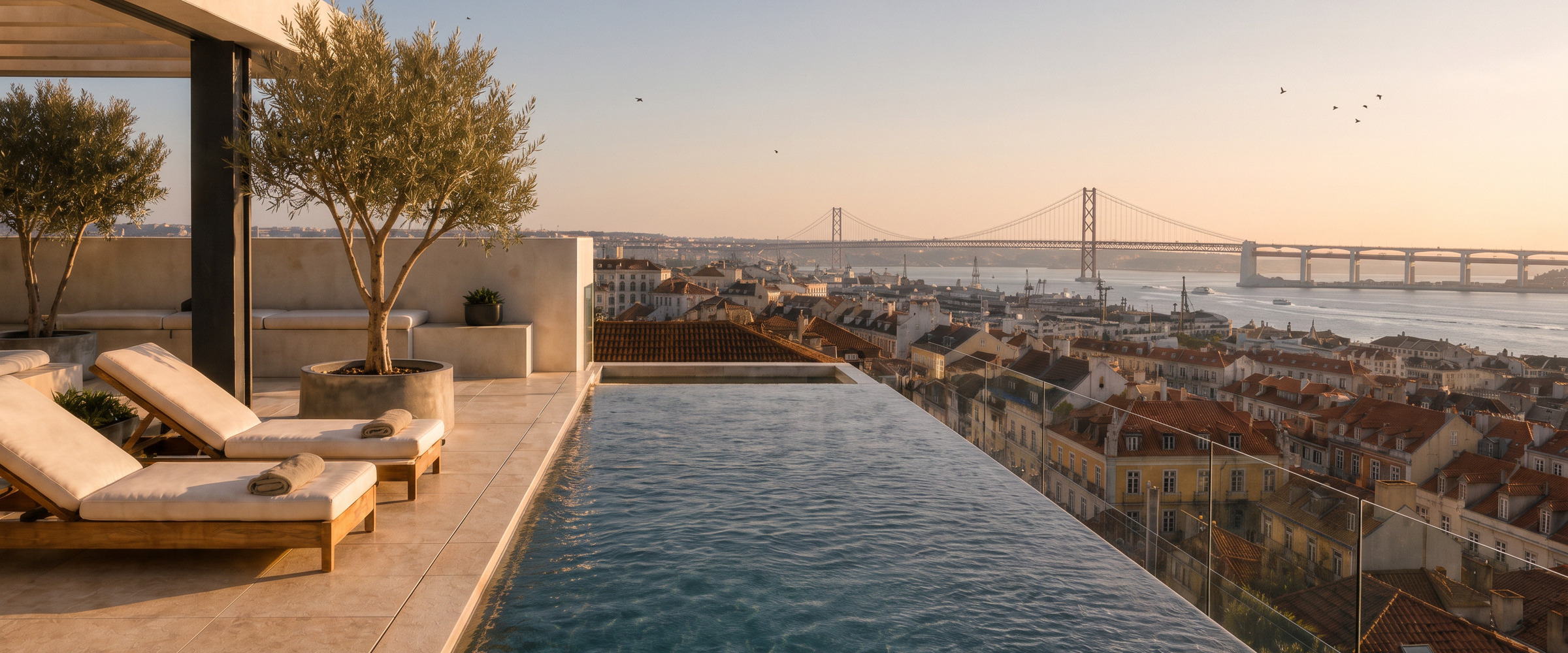 A rooftop pool at golden hour, looking across the Lisbon rooftops to the Tagus and the 25 de Abril bridge.